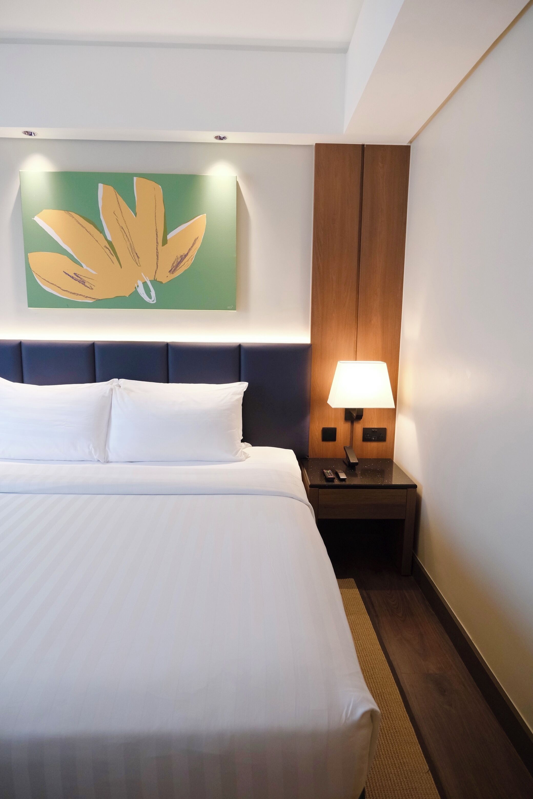 A hotel room with a large bed, a nightstand with a lamp, and a wall-mounted painting.