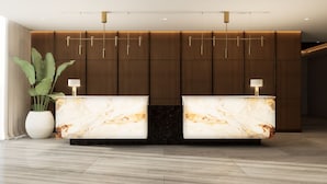 Un mostrador de recepción con encimeras de mármol, una planta en maceta grande y un panel de pared de madera moderna.
