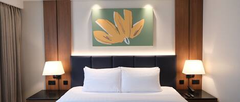 A hotel room with a large bed, two bedside tables with lamps, a wall-mounted artwork, and a headboard with built-in lighting.