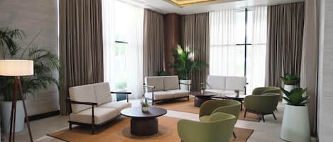 A modern hotel lobby with a sofa set, armchairs, a coffee table, and potted plants.