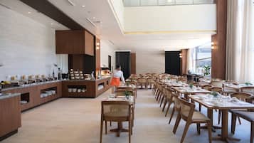 A spacious dining area with multiple tables and chairs, a buffet counter with various food items, and a modern interior design.