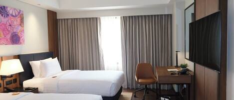 A hotel room with two beds, a desk, a chair, a TV, and a painting on the wall.