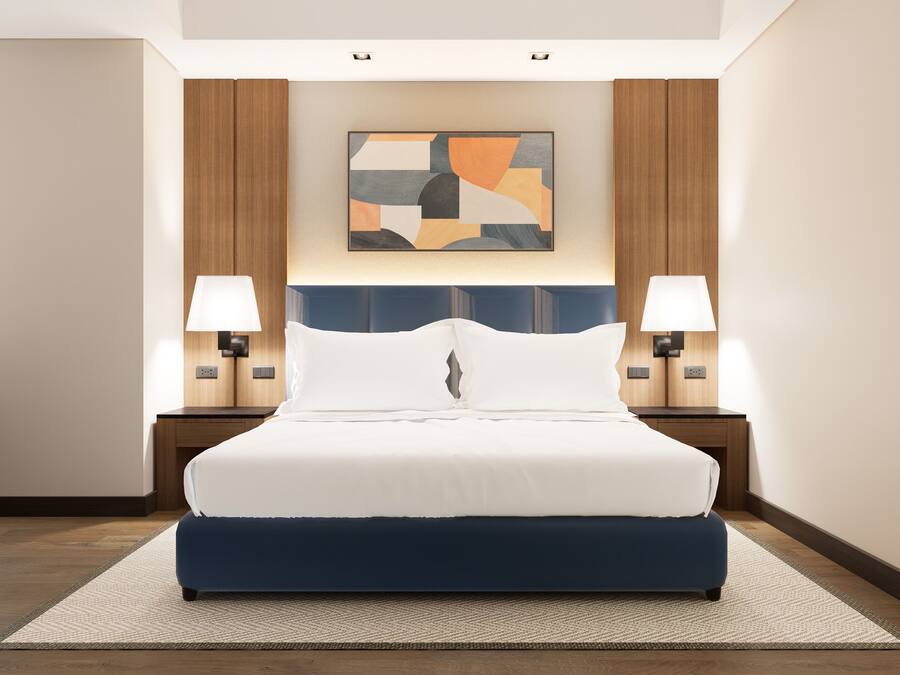 Een hotelkamer met een groot bed, twee bedlampen, een modern abstract schilderij en een stoel.