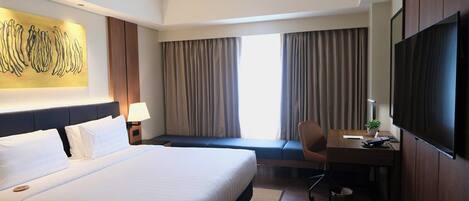 A hotel room with a large bed, a desk with a chair, a TV, and a window with curtains.