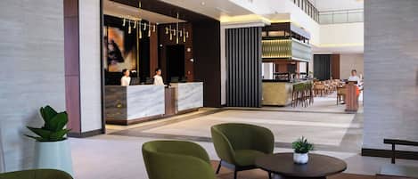 A modern lobby with a reception desk, seating area, and a staircase leading to an upper level.