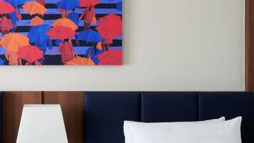A hotel room with a bed, a nightstand with a lamp, and a wall-mounted painting of umbrellas.