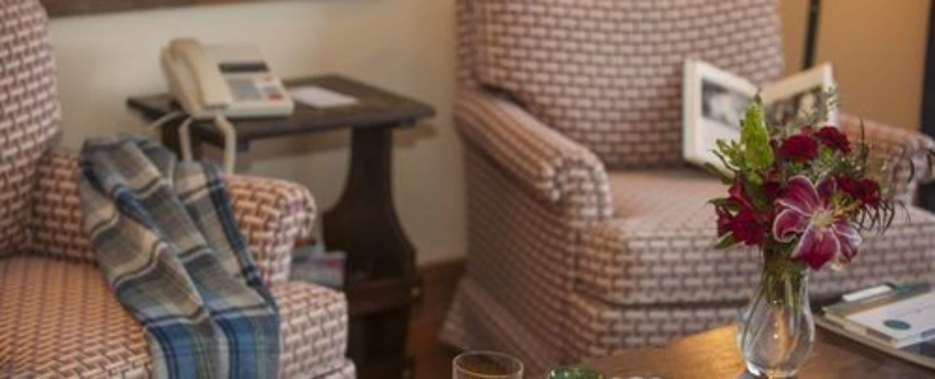 Una habitación con muebles con motivos, un florero con flores y una mesita con un teléfono y papeles.