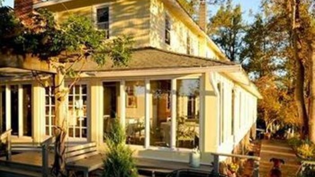 A two-story house with a porch, a covered outdoor seating area, and a dog in the yard. - The Orchard Inn (Saluda)