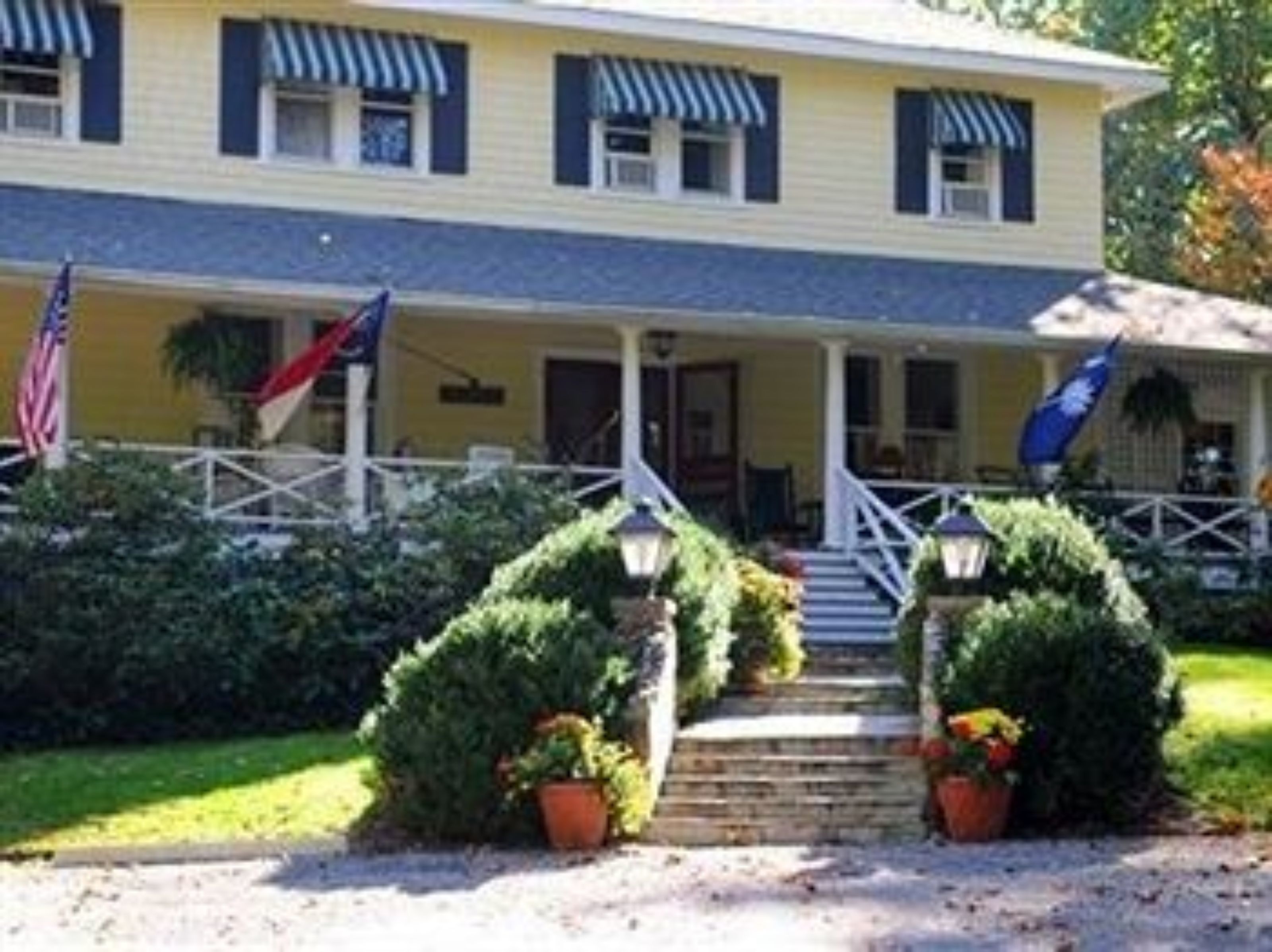 Una casa de dos pisos con un porche, banderas estadounidenses y plantas en macetas.