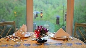 A dining table set for two with a view of a forested landscape through large windows. - The Orchard Inn (Saluda)