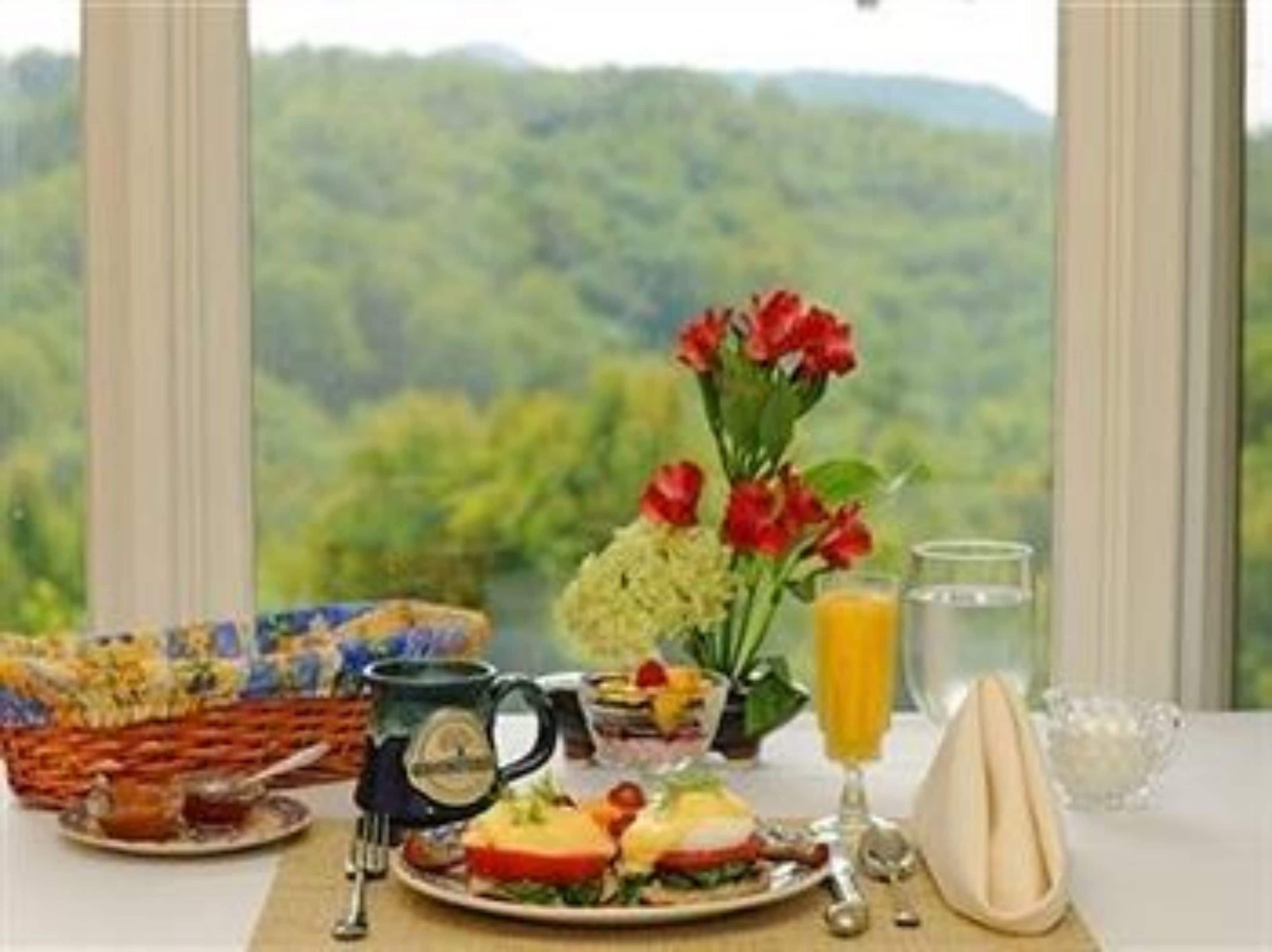 Una escena de desayuno con un plato de comida, una taza, un vaso de jugo de naranja y un florero con flores.