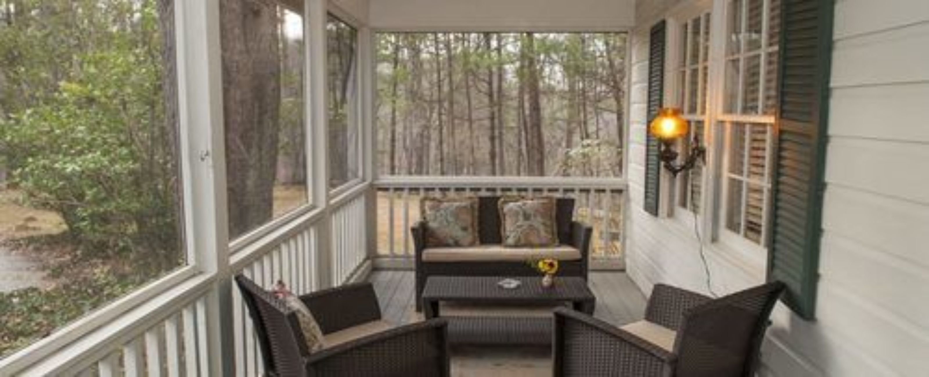 A covered porch with wicker furniture and a view of a wooded area.