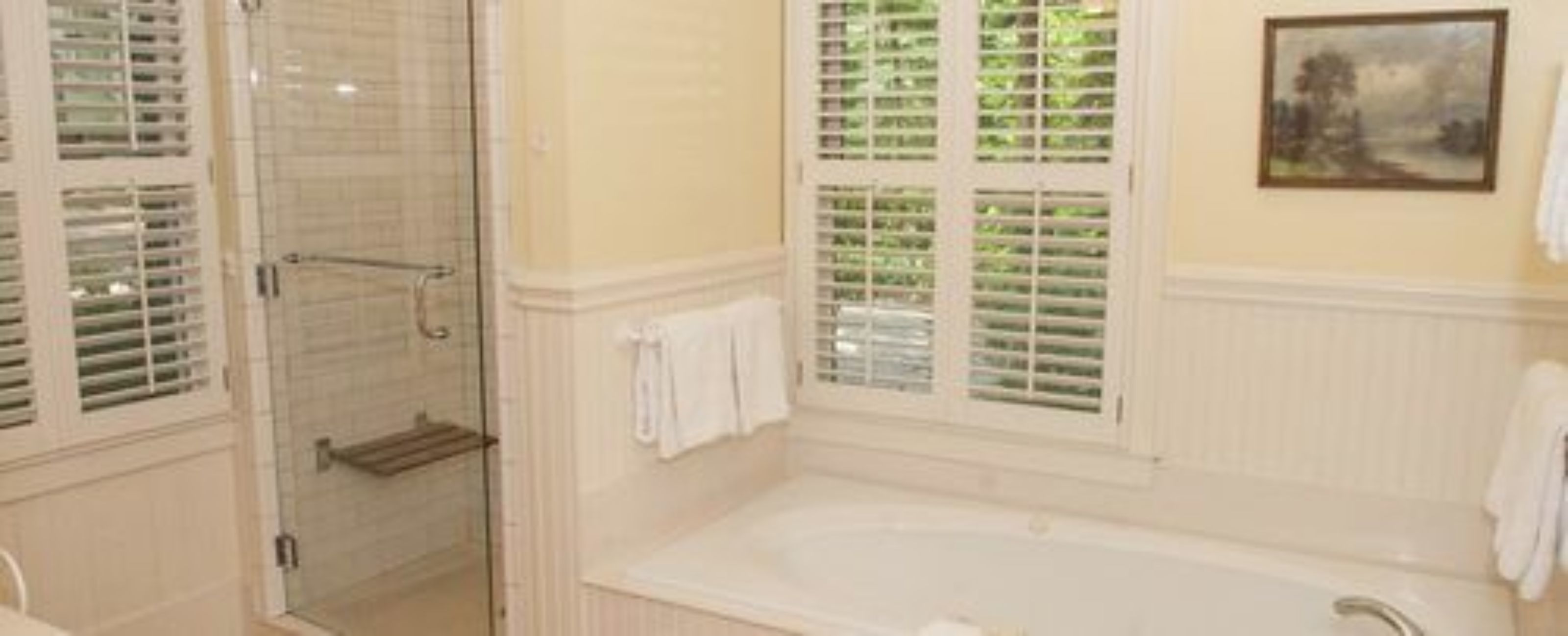A bathroom with a glass-enclosed shower, a bathtub, and a window with blinds.