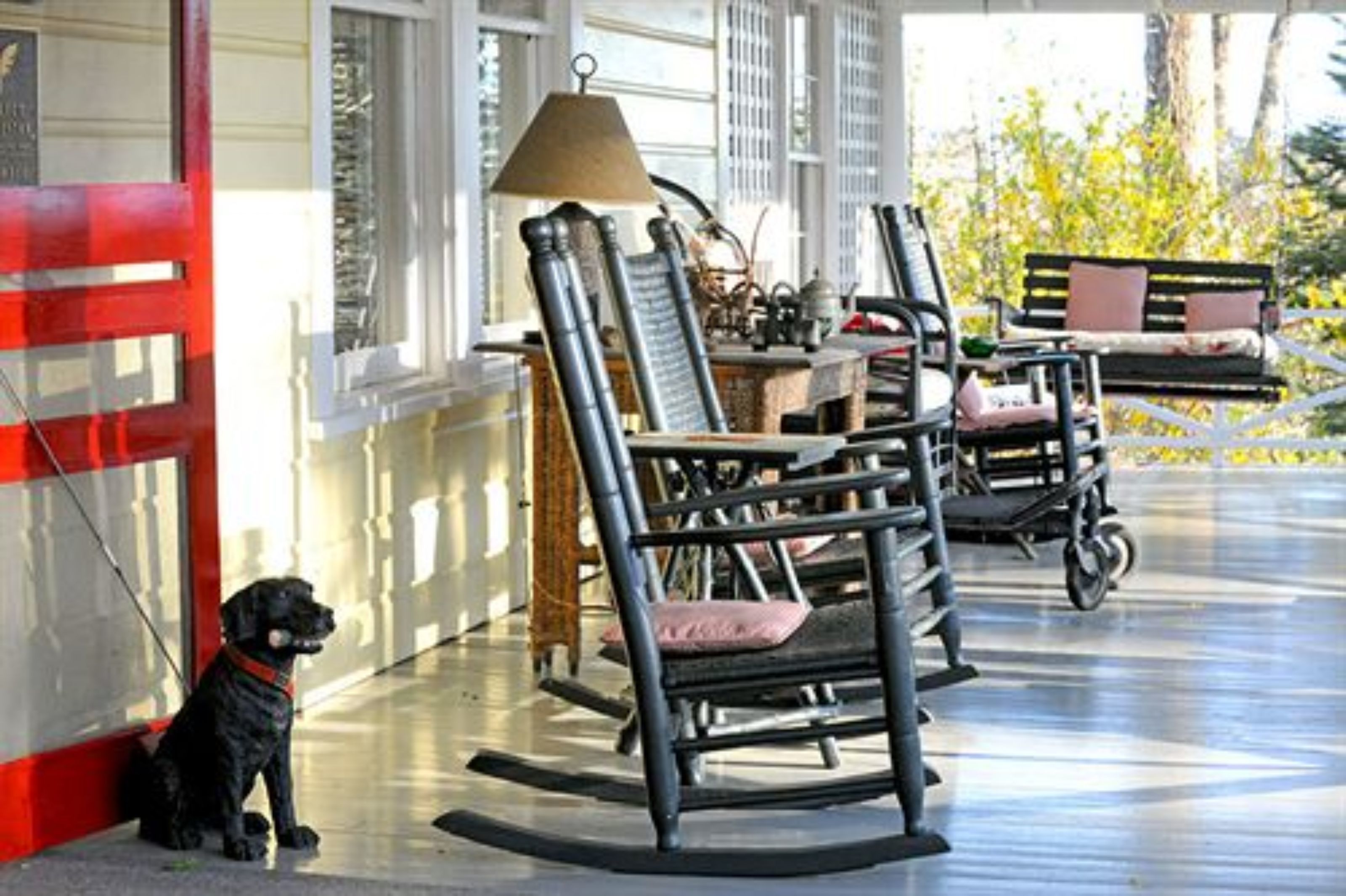 A porch with rocking chairs, a dog, and a lamp.