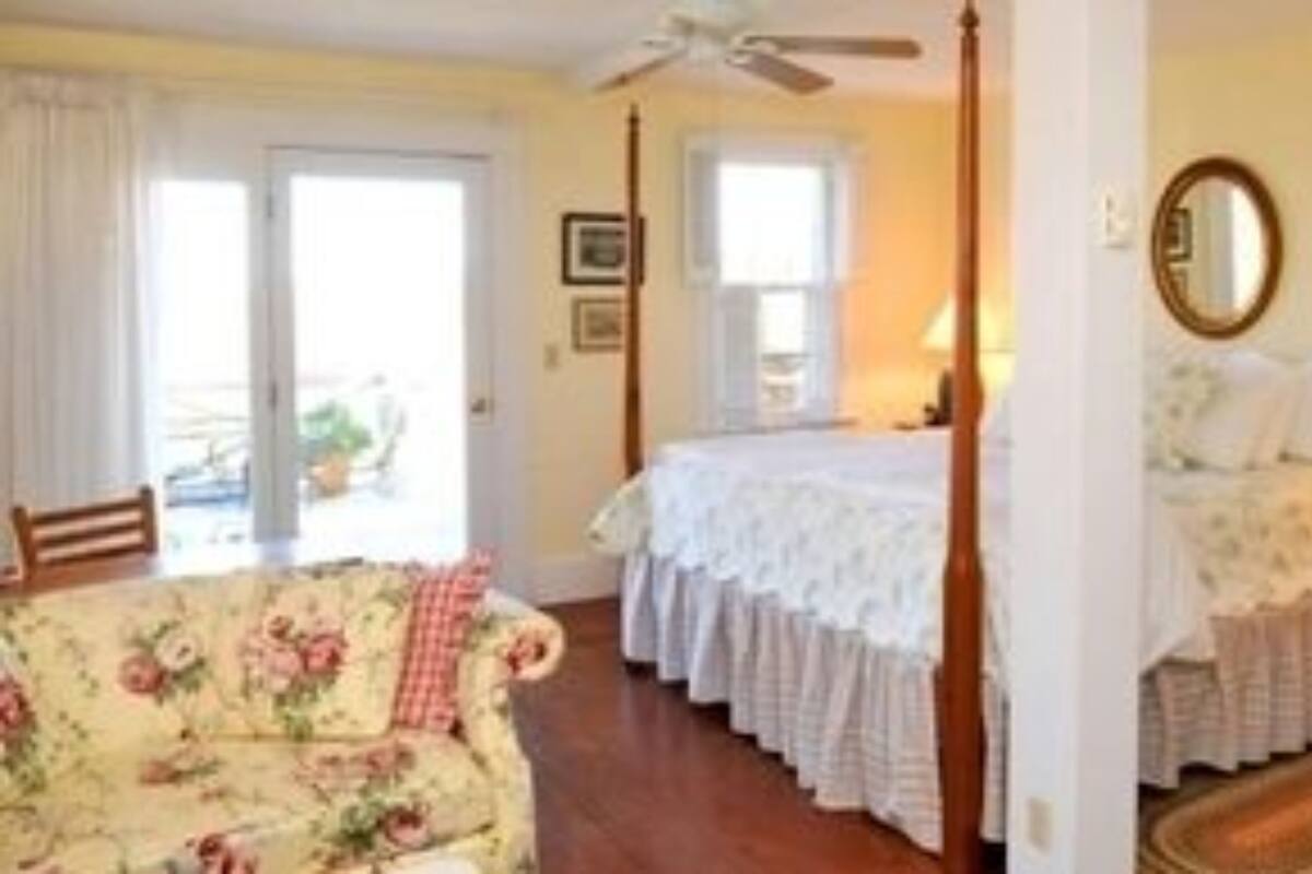 A bedroom with a four-poster bed, a sitting area with a floral sofa, and a view of the outdoors through a sliding door.