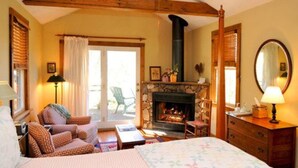 A cozy room with a fireplace, a bed, a sofa, and a wooden dresser. - The Orchard Inn (Saluda)