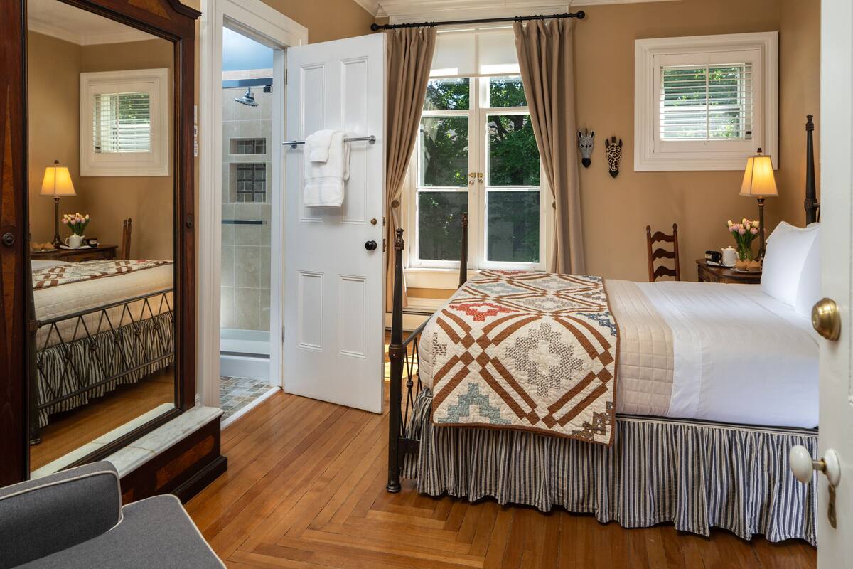 A bedroom with a large bed, a bathroom with a shower, and a view of the outdoors.