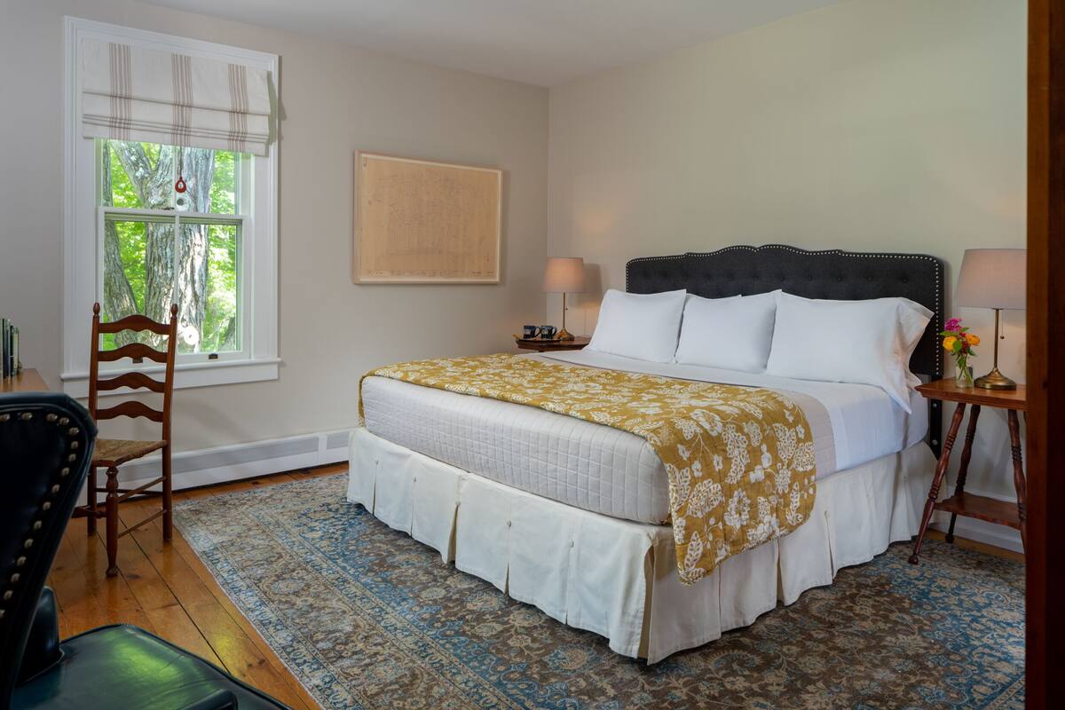 A bedroom with a large bed, a chair, a window with a view of trees, and a rug.