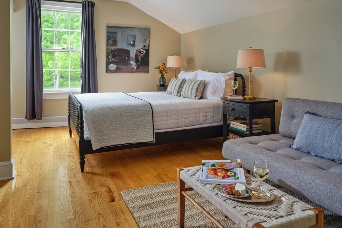 A bedroom with a bed, a sofa, a nightstand, a lamp, and a window with curtains.