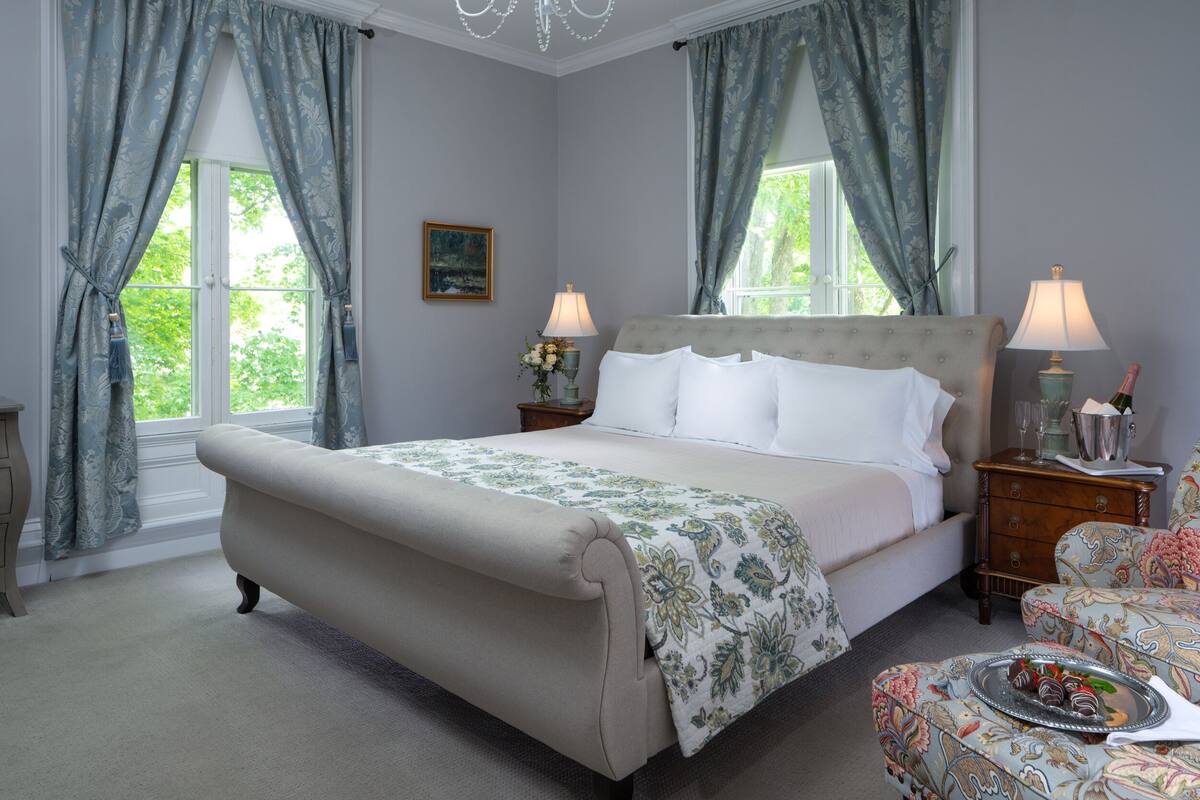 A bedroom with a large bed, two bedside tables, a nightstand, a chair, and a window with curtains.