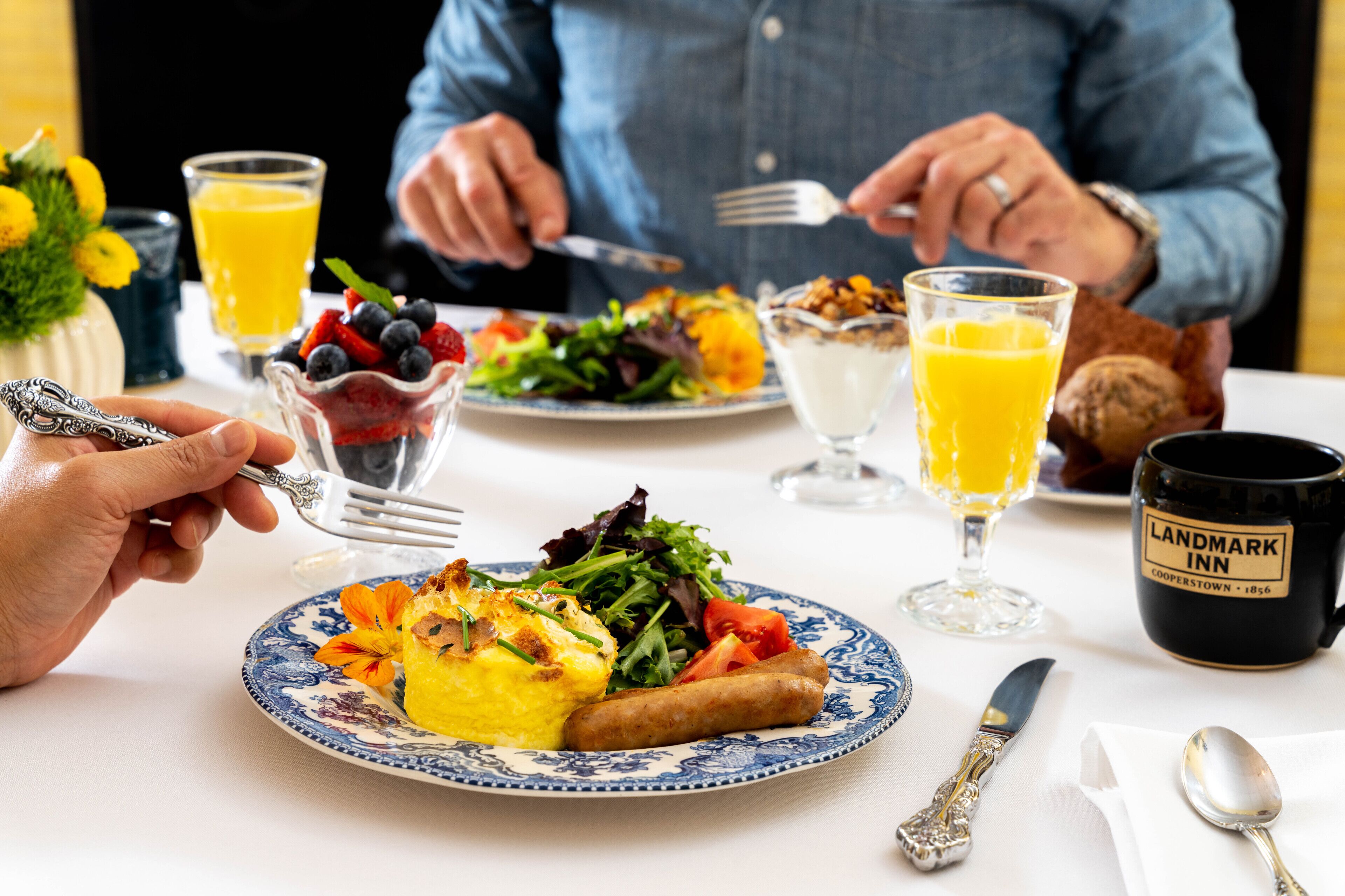 Een eettafel met borden eten, een glas sinaasappelsap en een mok met de tekst 'Landmark Inn'.