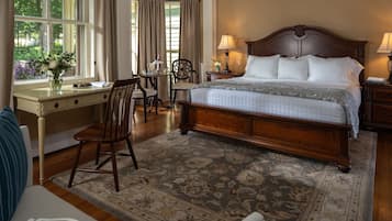 Una habitación de hotel con una cama grande, un escritorio con silla, una mesita pequeña y una ventana con cortinas.