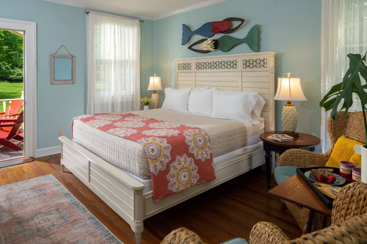 A bedroom with a bed, two bedside tables with lamps, a chair, a table with a tray, and a fish decoration on the wall.