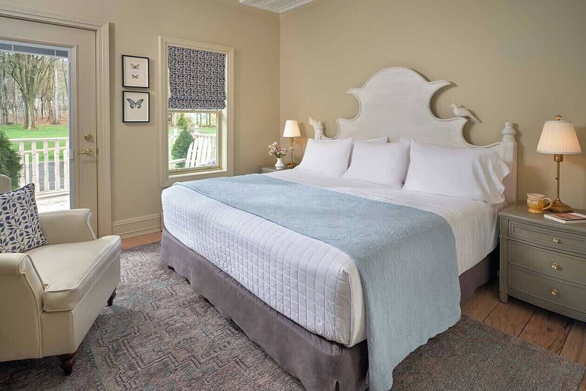 A bedroom with a large bed, a chair, a nightstand, and a window with a view of the outdoors.
