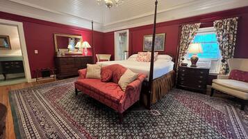 A four-poster bed with a canopy, a red sofa, and a patterned rug in a room with red walls and a chandelier.