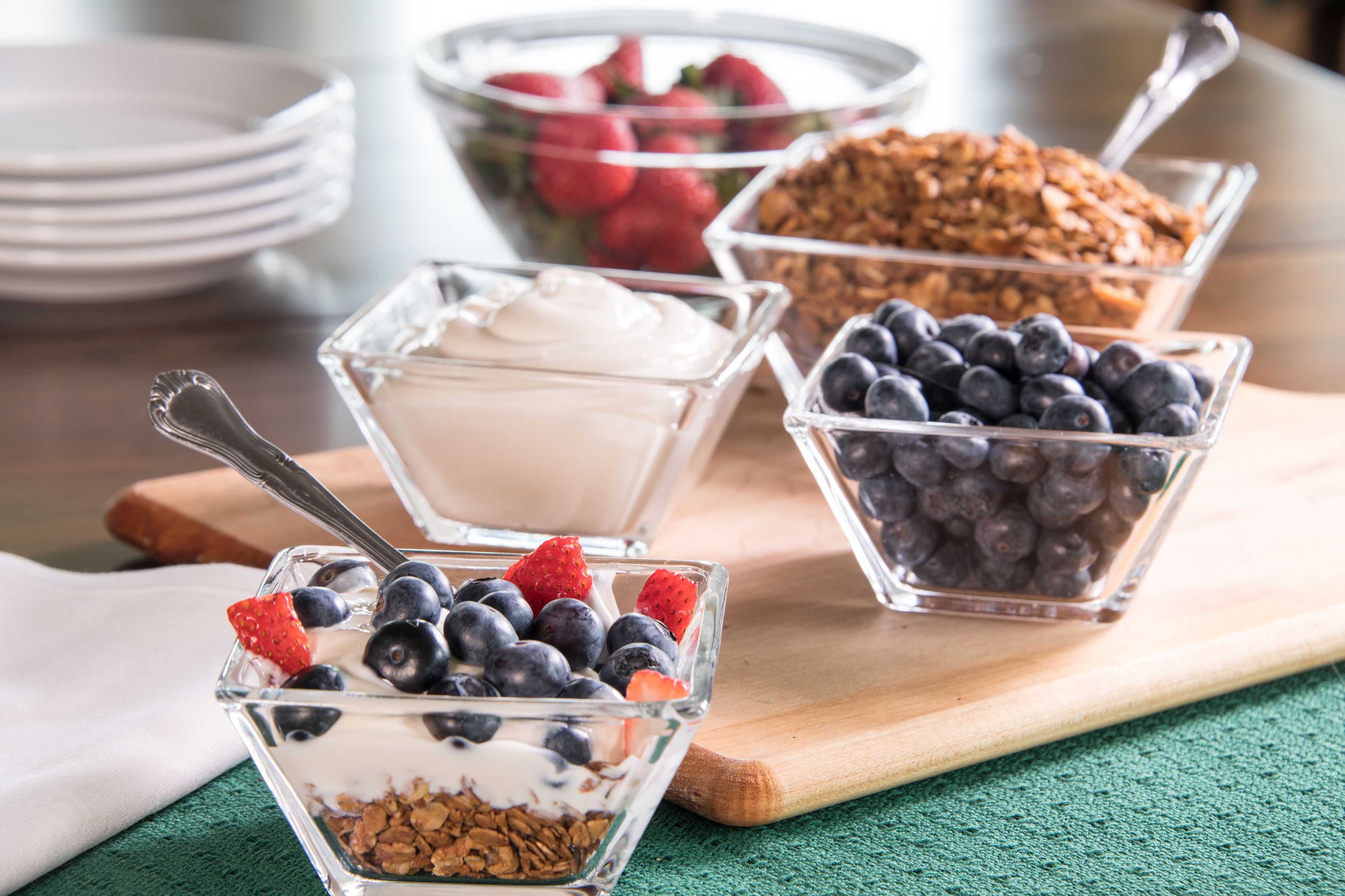 Three glass bowls containing yogurt, granola, and mixed berries on a wooden board.