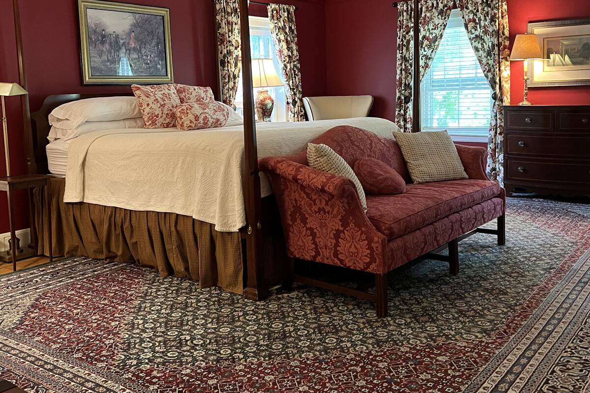 A room with a four-poster bed, a red sofa, a chandelier, and a large window with curtains.