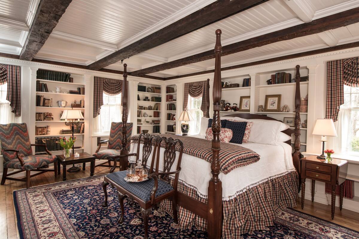 A traditional bedroom with a four-poster bed, a large bookcase, and a classic wooden floor.