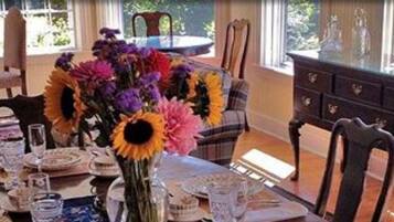 A dining area with a table set for a meal, a vase with flowers, and a view of the outdoors through large windows.
