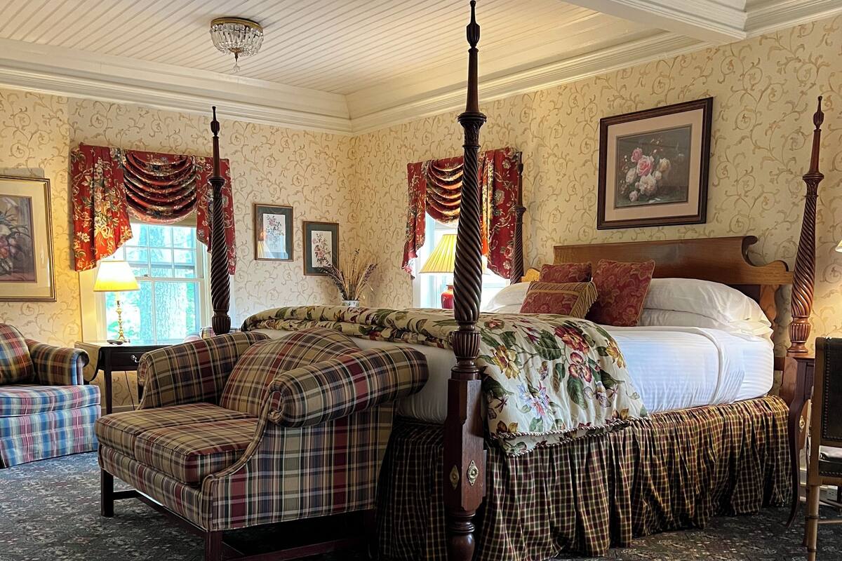 A traditional bedroom with a four-poster bed, a wooden bench, and a patterned carpet.