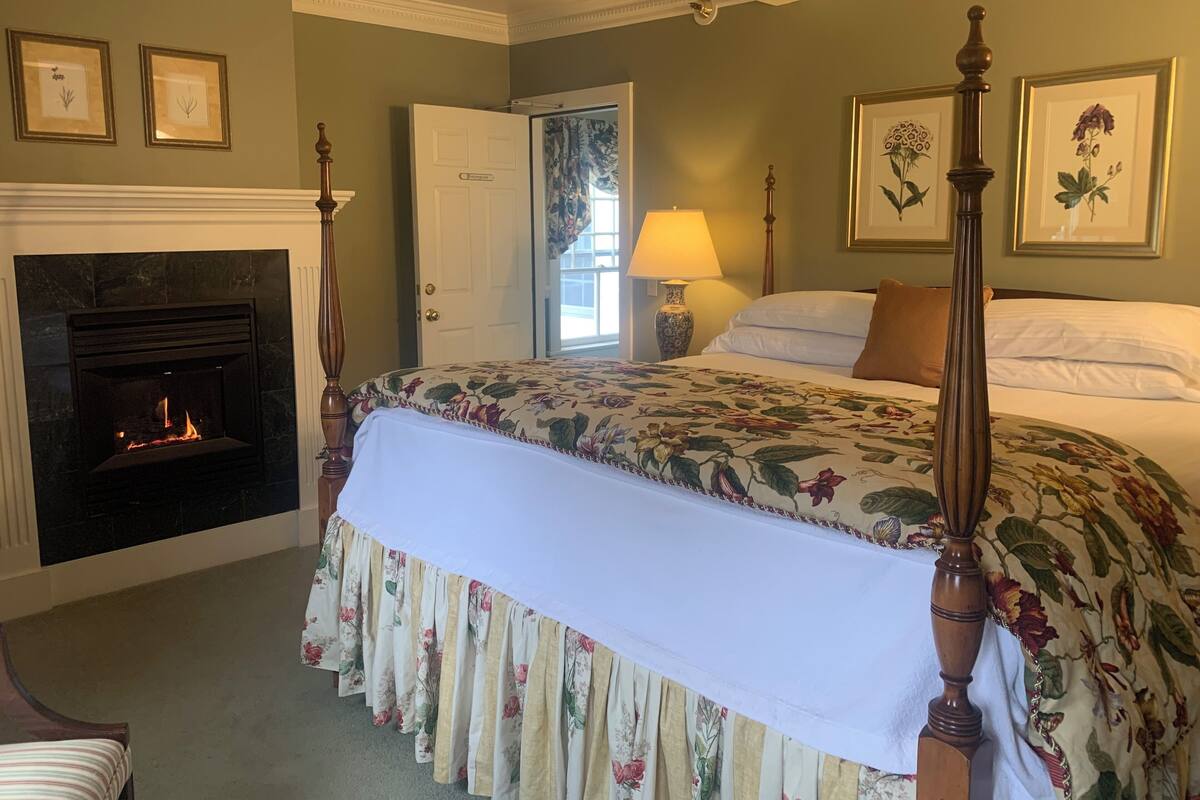 A bedroom with a four-poster bed, a fireplace, and floral wall art.
