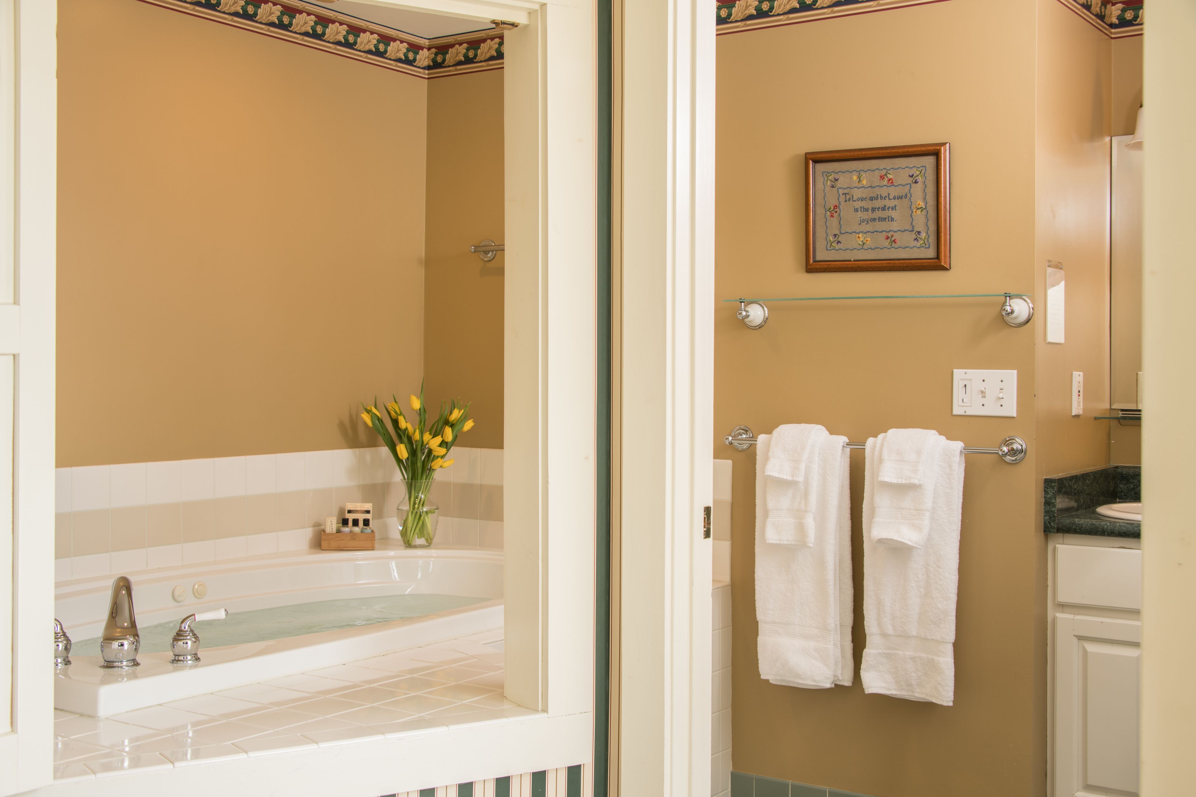 A bathroom with a bathtub, a towel rack with two towels, and a framed quote on the wall.