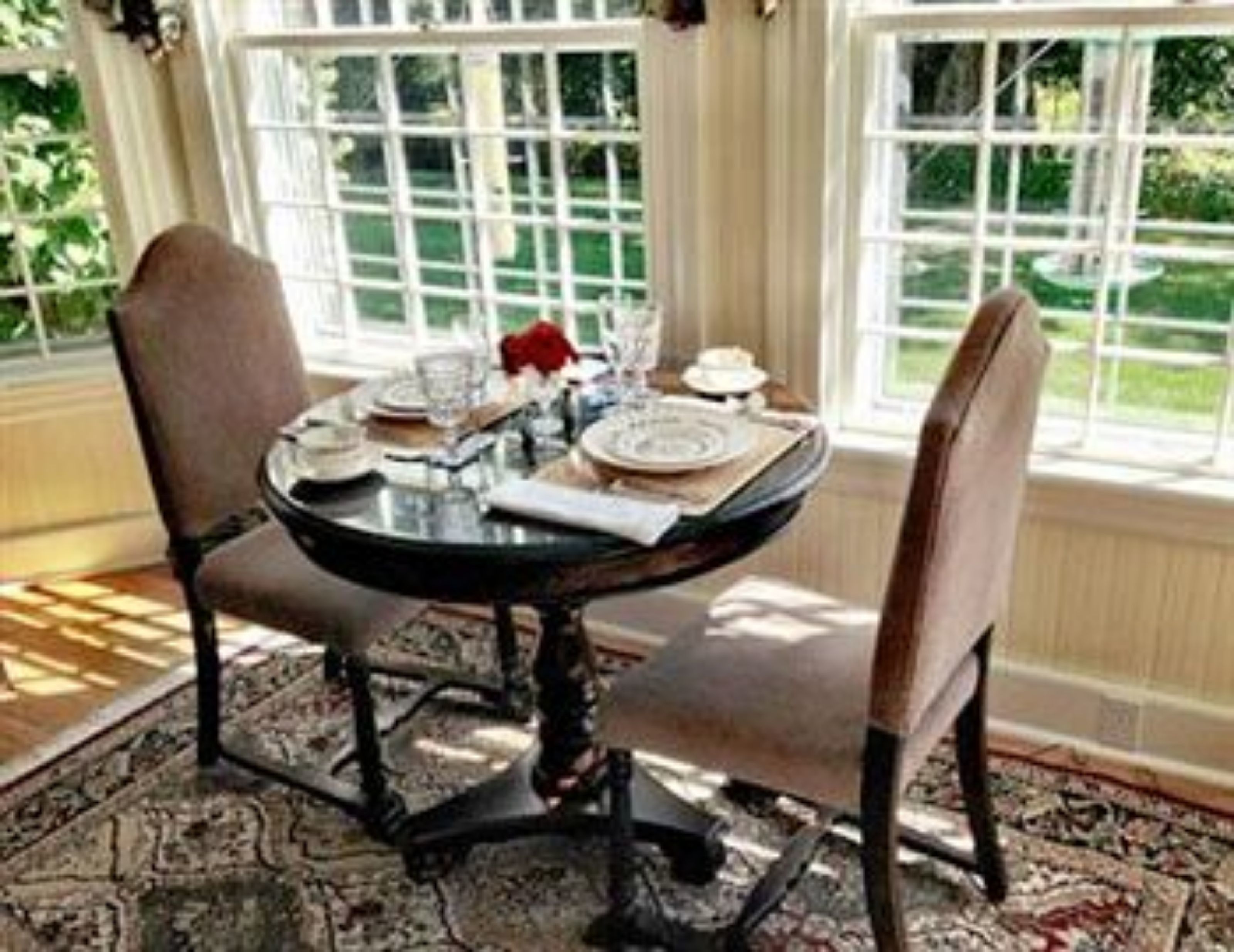 A round dining table with chairs, set with plates, glasses, and a vase of flowers.