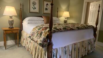 A four-poster bed with floral bedding, two bedside lamps, and framed botanical prints on the wall.