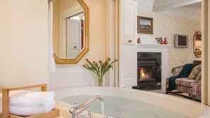 Une salle de bain avec une grande baignoire, un miroir avec un cadre doré et une chaise en bois sur laquelle est posée une serviette.
