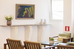 A dining area with a table, chairs, a vase with flowers, a framed abstract painting, and a window with a view. - Athinais Hotel (Athens)