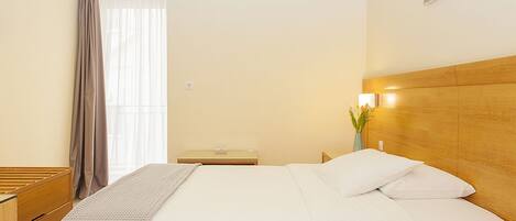 Una habitación de hotel con una cama grande, cabecera de madera, mesitas de noche, una lámpara y un ventanal con cortinas.