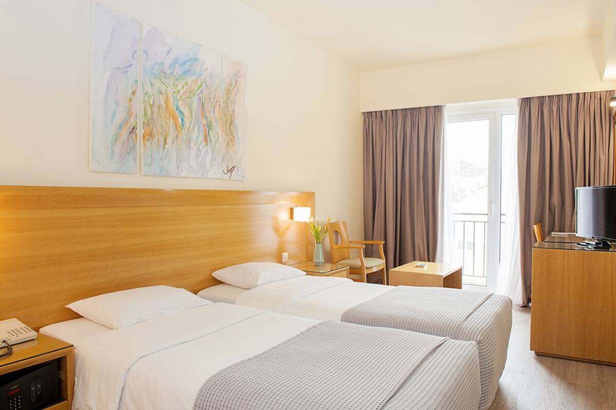 A hotel room with two beds, a desk, a TV, and a painting on the wall.