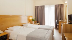 A hotel room with two beds, a desk, a chair, a TV, and a bedside table with a lamp. - Athinais Hotel (Athens)