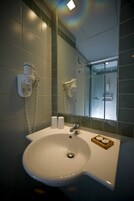 Ένα μπάνιο με νιπτήρα, δύο συσκευές στεγνώματος χεριών και ένα διαχωριστικό ντους από γυαλί.