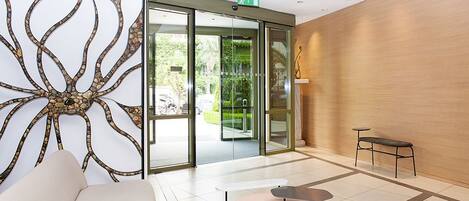 A modern lobby with a glass door entrance, a seating area with a sofa and tables, and a decorative wall panel.