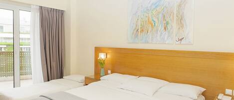 A hotel room with a large bed, a bedside table with a lamp, a phone, and a window with curtains.