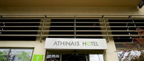 The entrance to Athinais Hotel with a modern facade and a sign indicating the cafe opens at 8am.