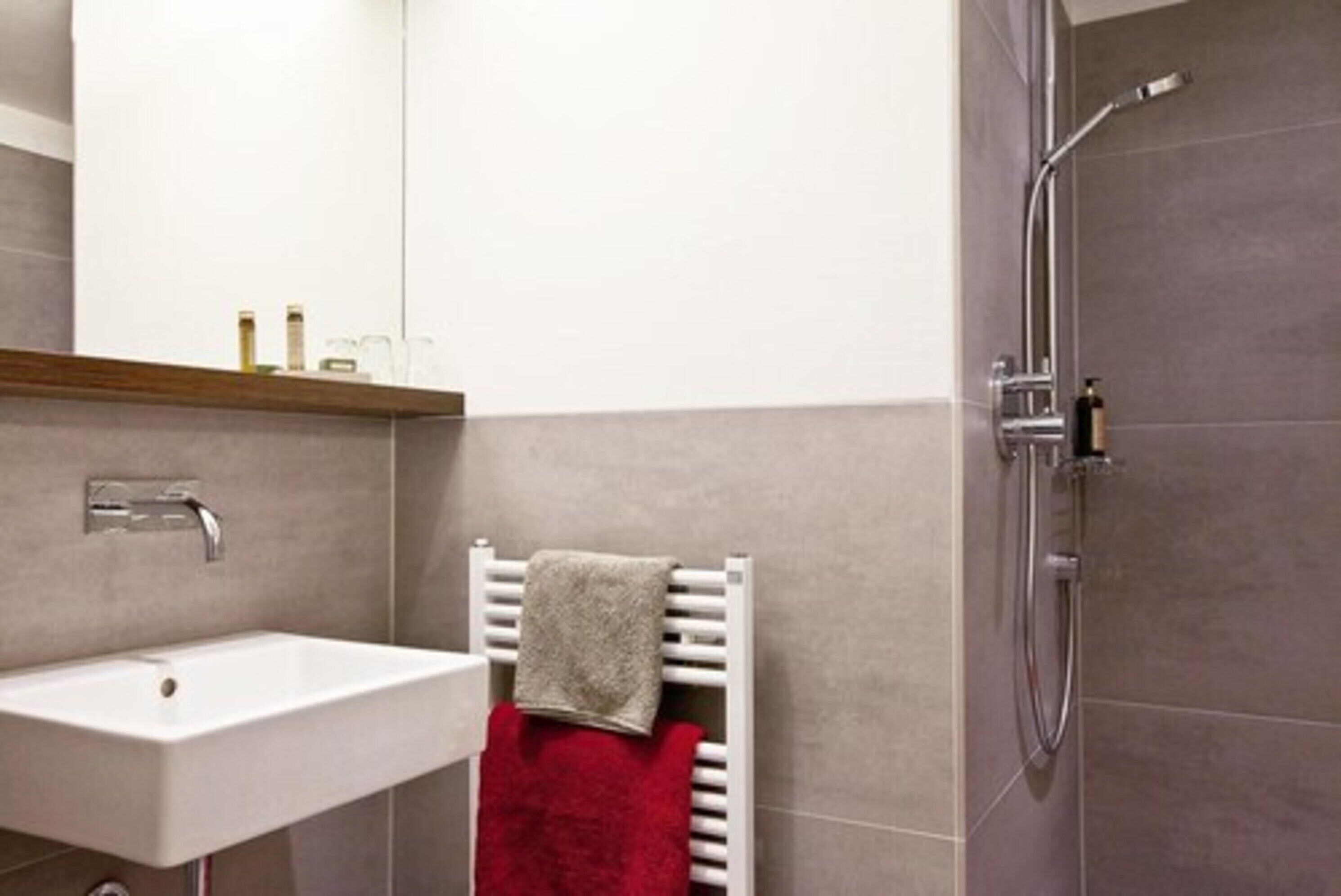 Un baño moderno con un lavamanos blanco, un toallero con una toalla roja y una zona de ducha.