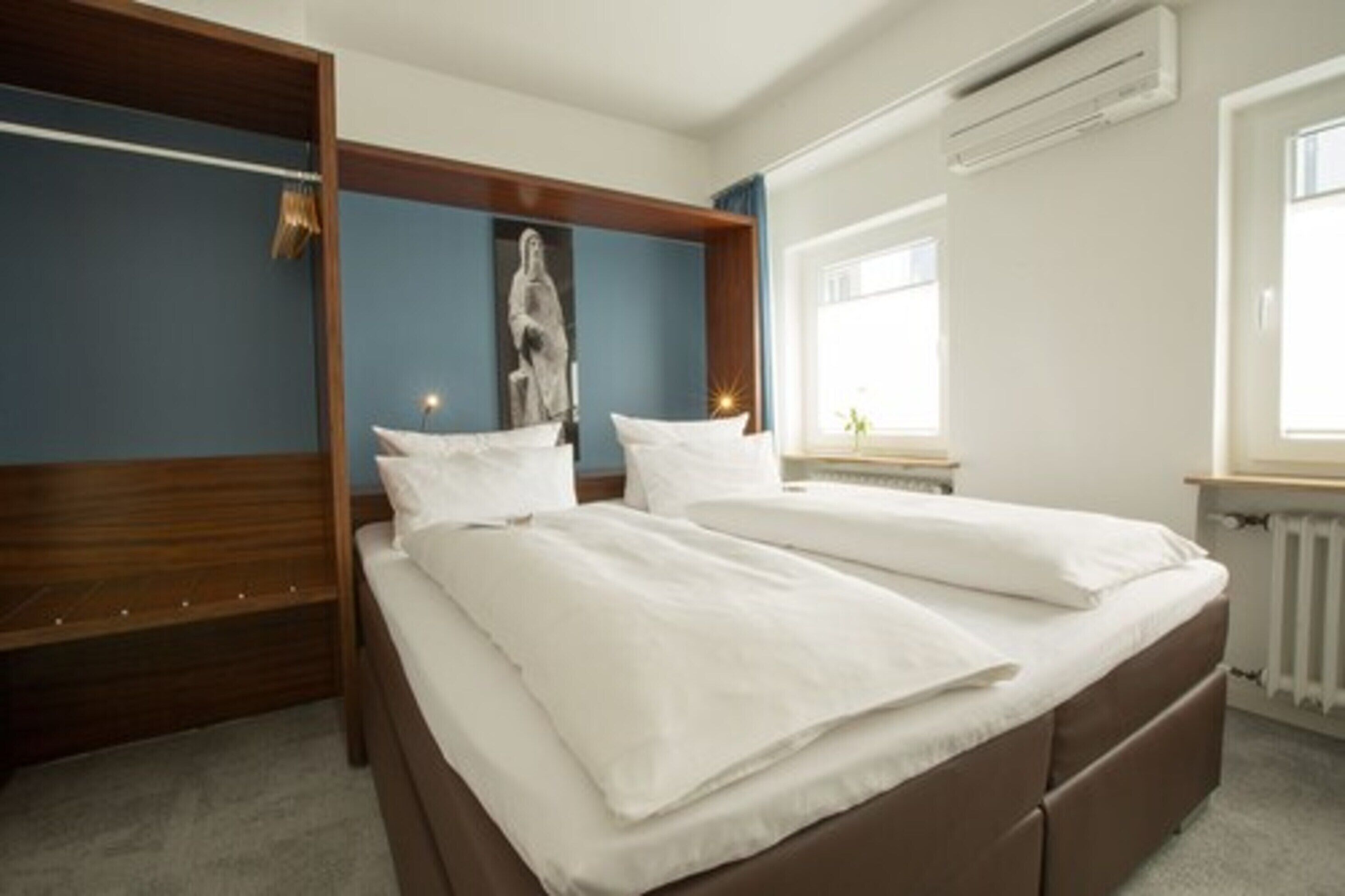 A bedroom with a double bed, a wooden headboard, a wall-mounted air conditioner, and a window with daylight.