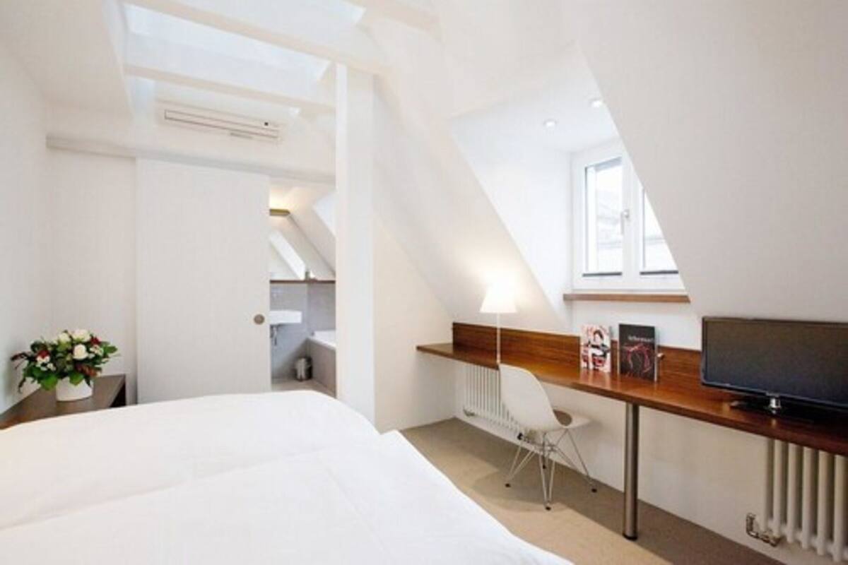 Quarto de hotel moderno com uma cama grande, uma escrivaninha com cadeira, televisão e um claraboia.
